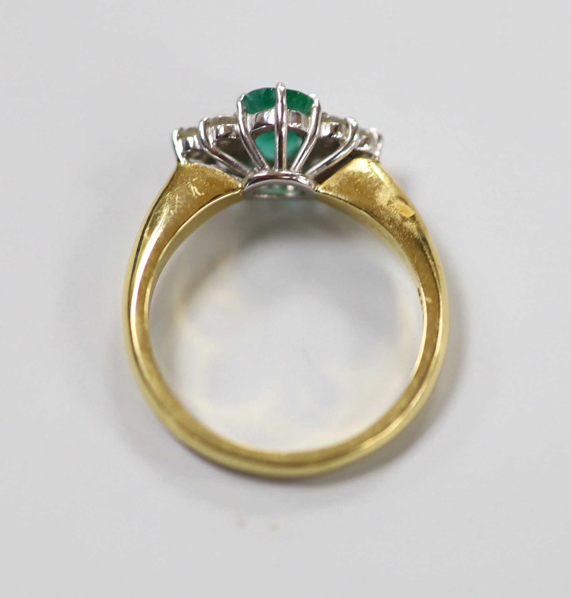 A modern 18ct gold and single stone oval cut emerald set ring, with six stone diamond chip set shoulders, size N/O, gross weight 4.8 grams.